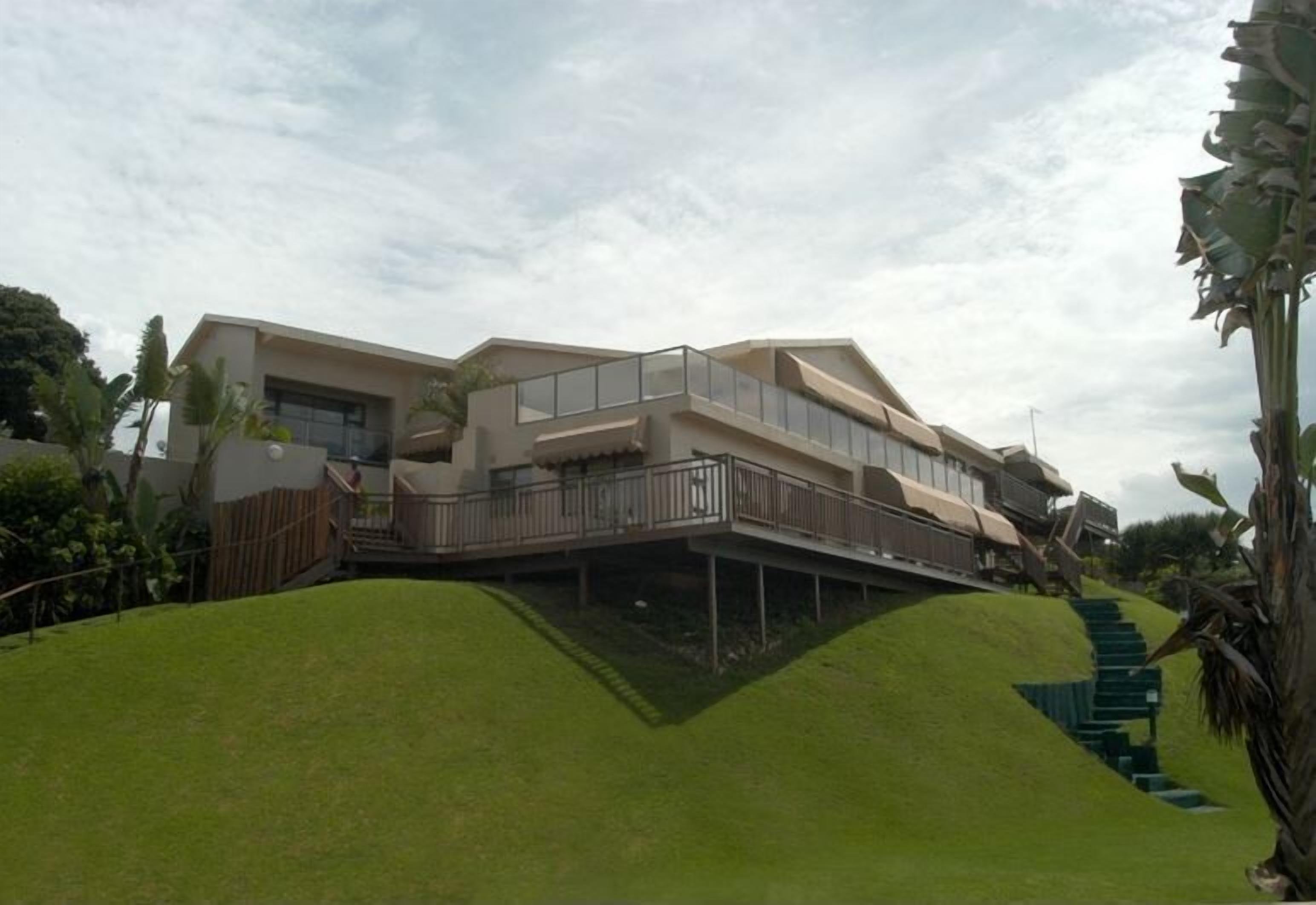 Une maison moderne avec un toit plat, un grand balcon et un escalier menant à l’entrée.