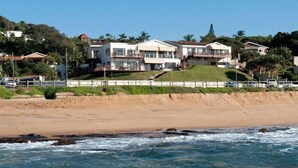 A beachfront property with multiple houses, a sandy beach, and ocean waves. - Fairlight Beach House (eMdloti)