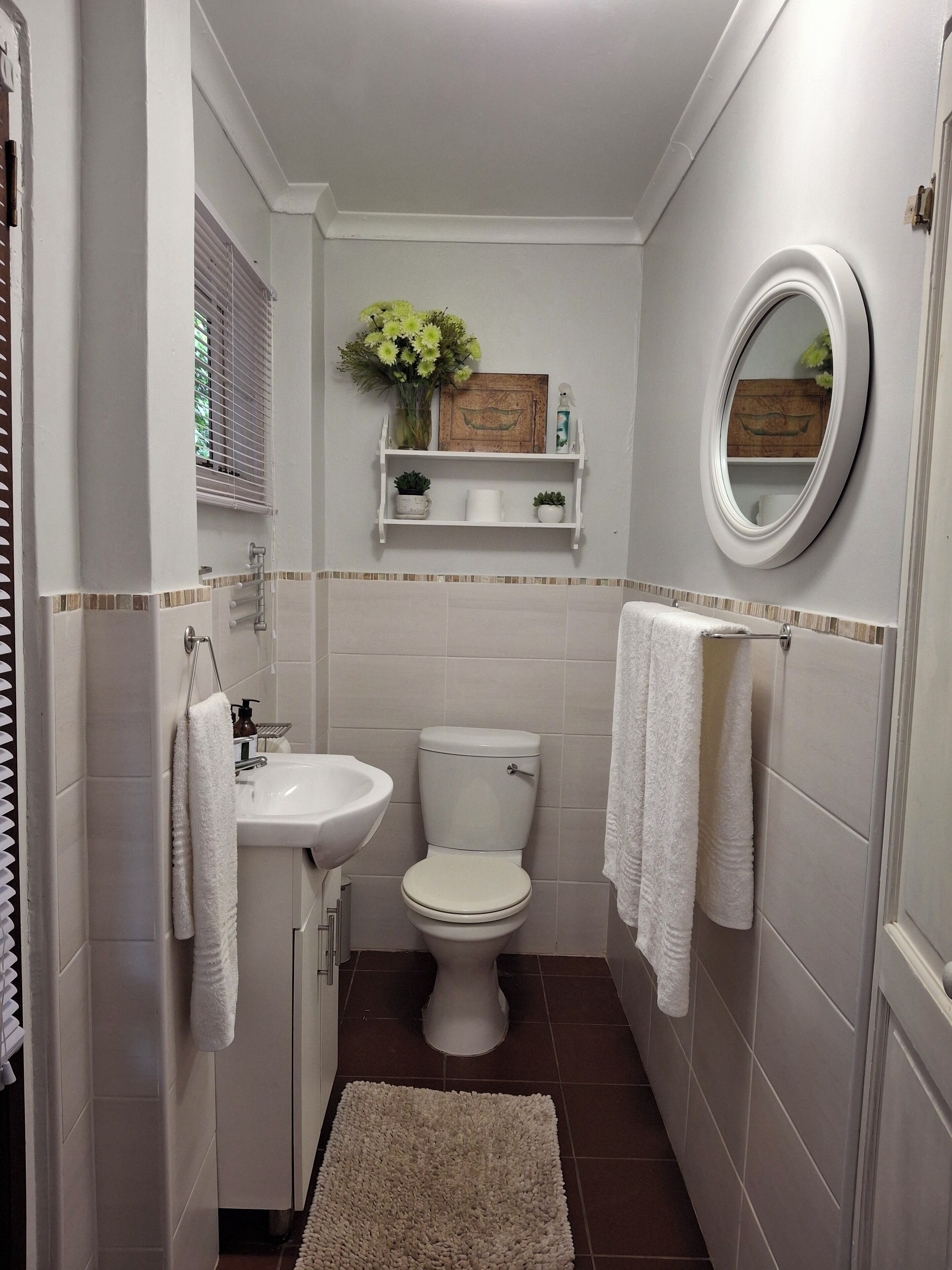 A bathroom with a toilet, sink, and mirror. There are towels hanging on the wall and a rug on the floor.
