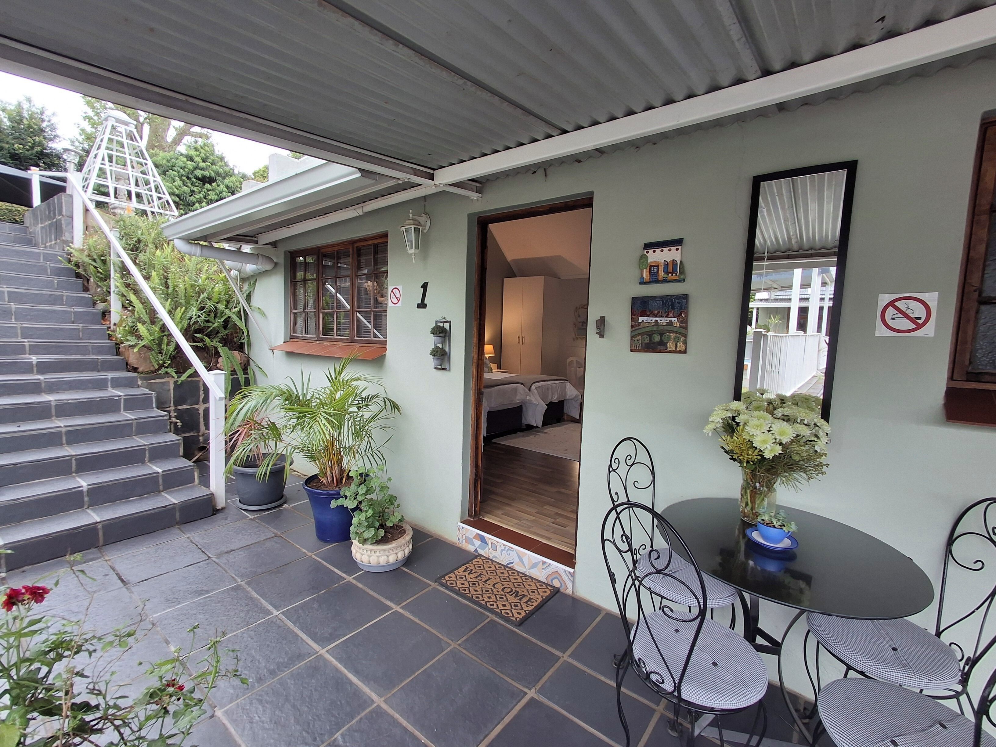 A covered patio with a dining table and chairs, potted plants, and a staircase leading to an upper level.