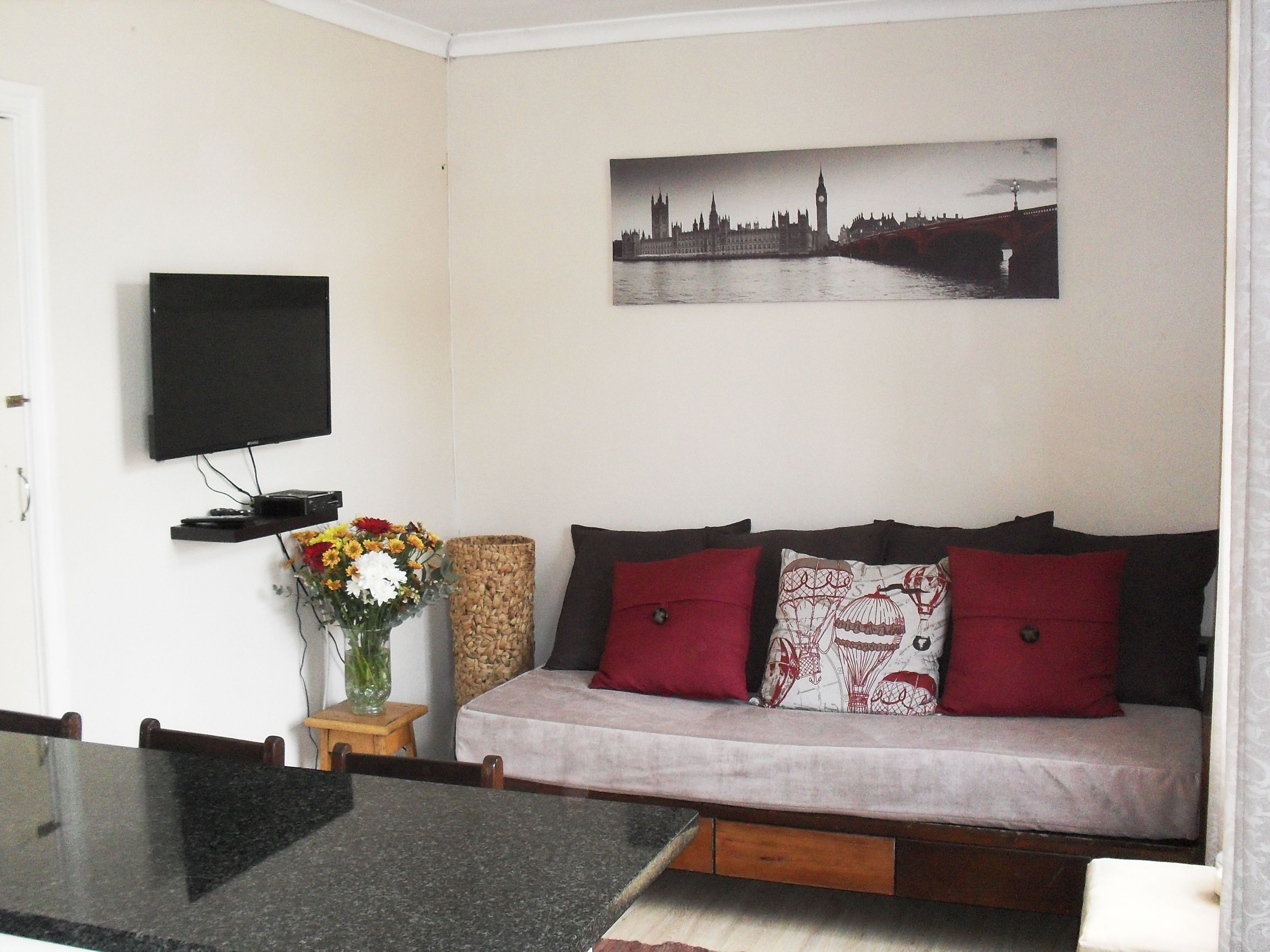 Una sala de estar con un sofá, un televisor de pantalla plana, un florero con flores y un cuadro de un paisaje urbano en la pared.