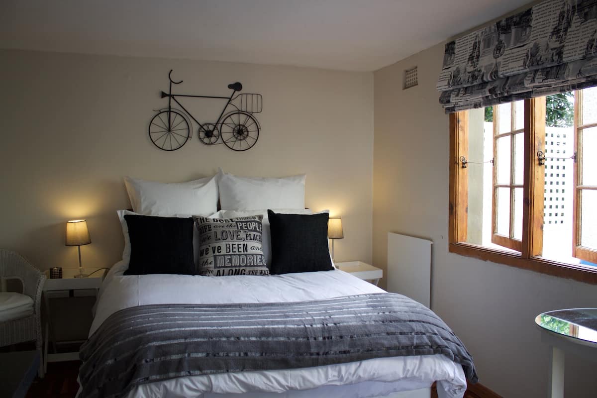 A neatly made bed with a striped blanket, two bedside lamps, a wall-mounted bicycle decoration, and a window with a view of the outside.