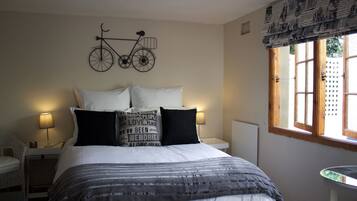 A neatly made bed with a striped blanket, two bedside lamps, a wall-mounted bicycle decoration, and a window with a view of the outside.