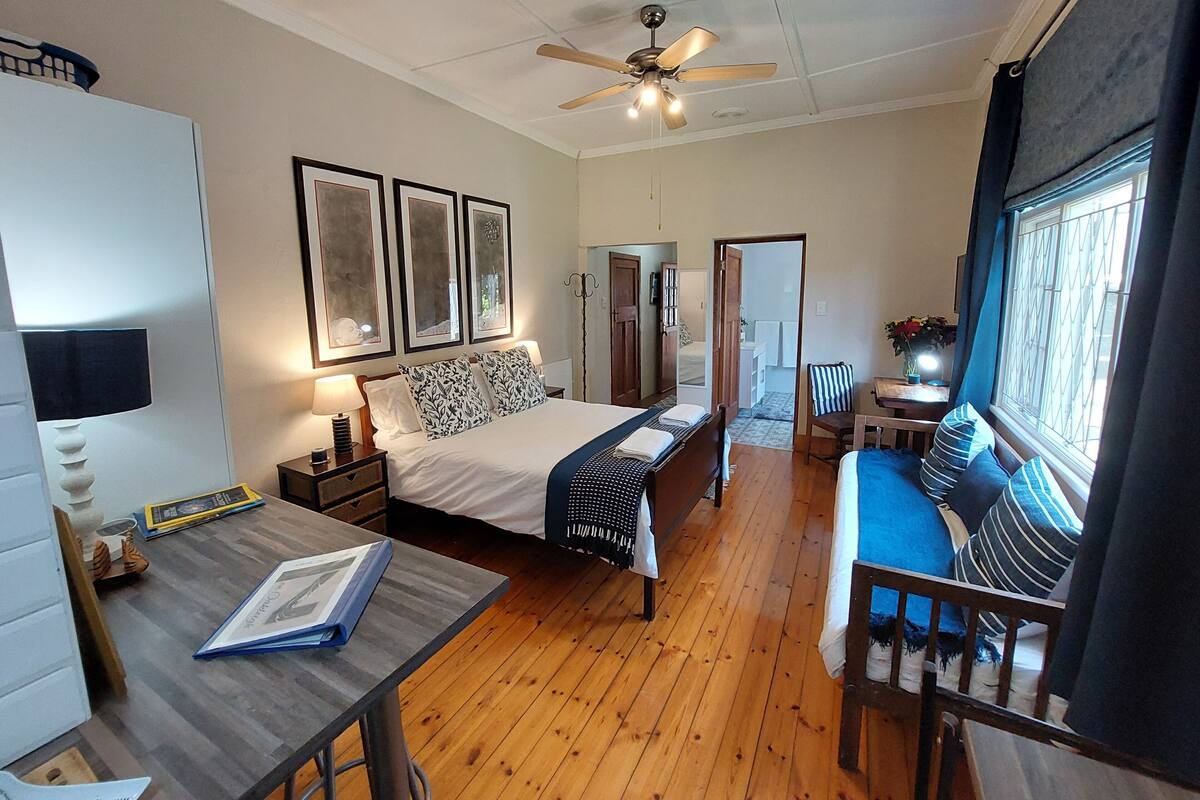 A bedroom with a bed, bedside tables, a desk, a chair, a ceiling fan, and a window with curtains.