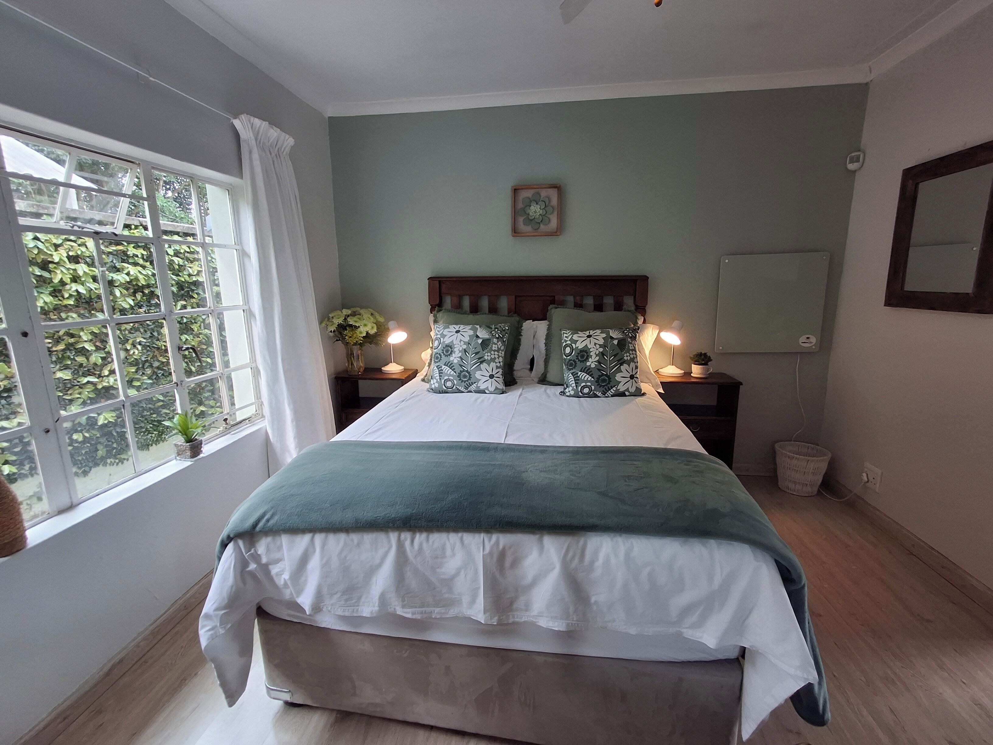 Un dormitorio con cama, lámparas de noche, mesita de noche, ventana con cortinas y vistas al exterior.
