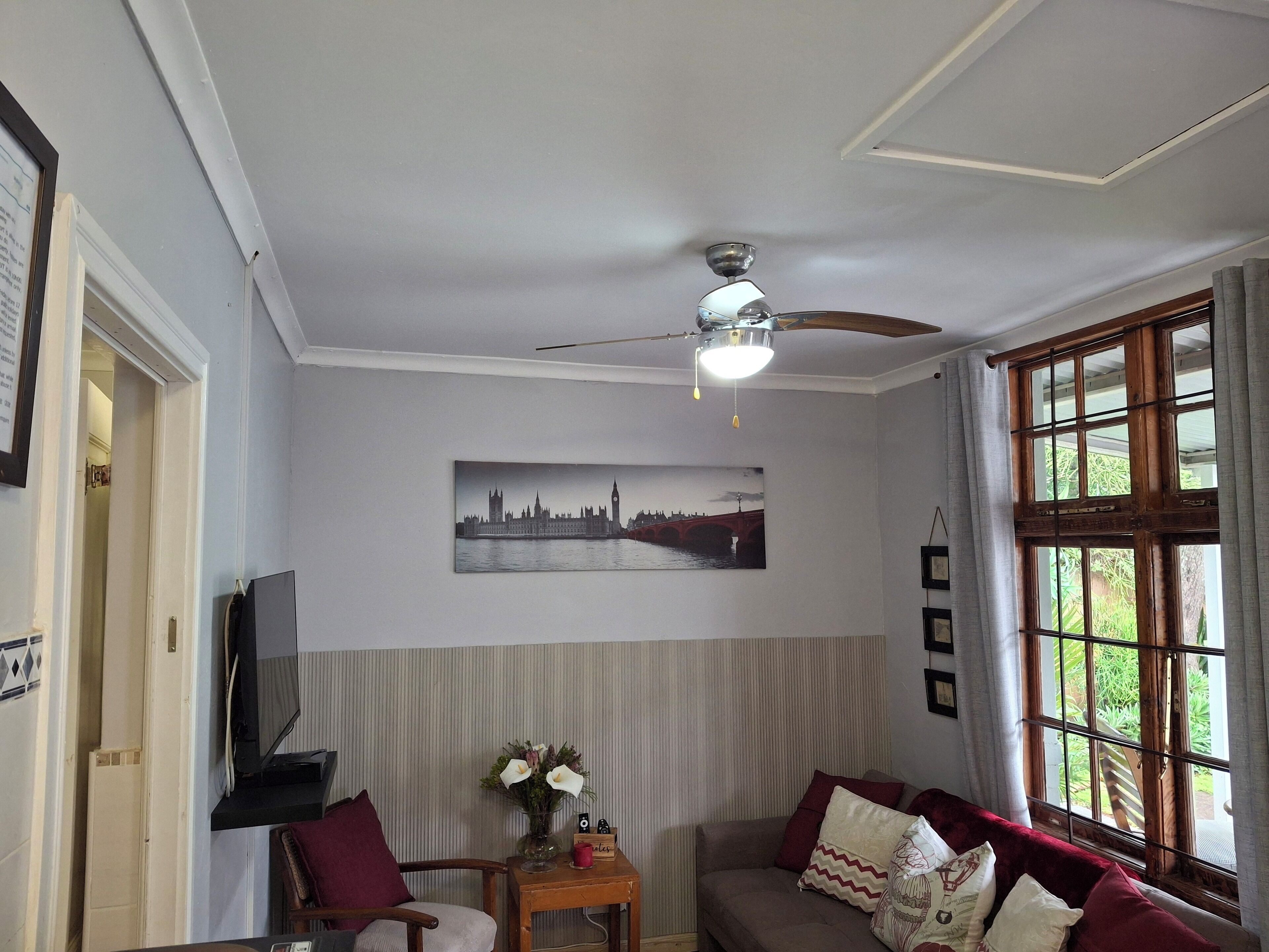 Una sala de estar con ventilador de techo, televisor, sofá, sillón y ventana con cortinas.
