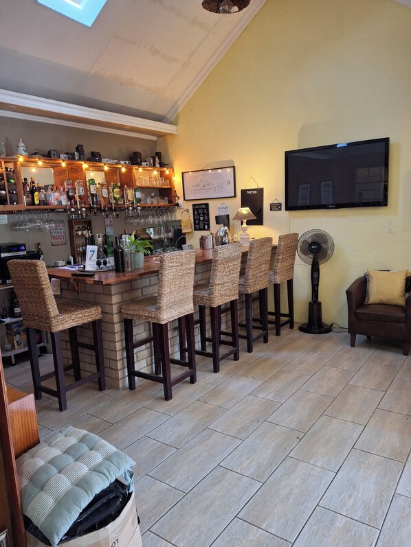 A bar area with a counter, bar stools, a television mounted on the wall, and a fan.
