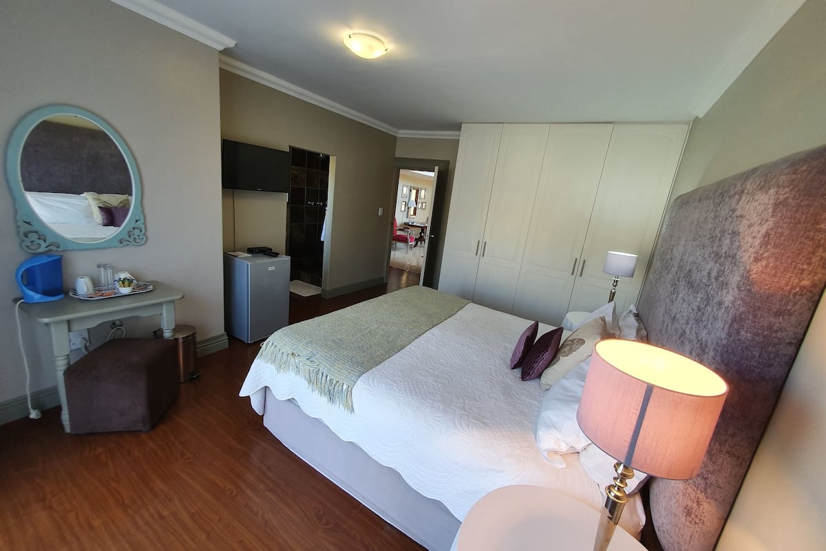 A hotel room with a bed, a desk, a mirror, a wardrobe, and a bathroom visible through an open door.