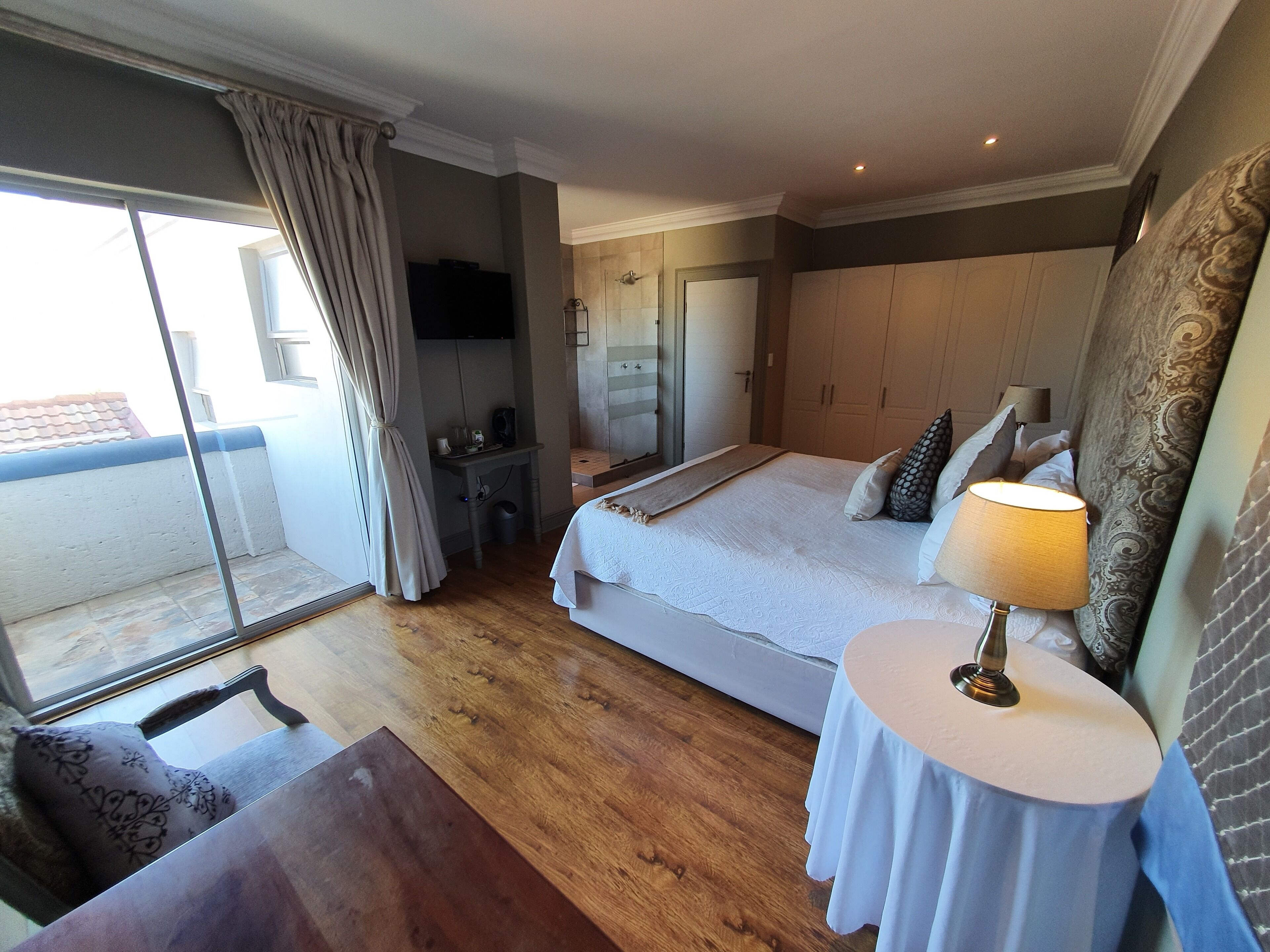 A hotel room with a large bed, a desk, a chair, a TV, and a window with curtains.