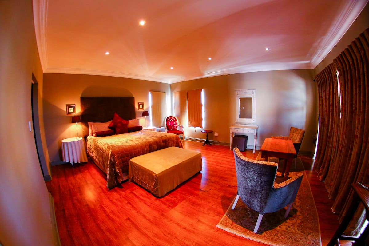 A spacious bedroom with a large bed, a sitting area with a chair and table, and a small fireplace.