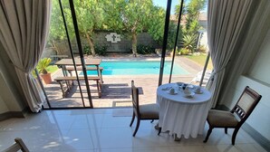 Un comedor con una mesa dispuesta para dos, vista a la piscina y una decoración mural en forma de cruz.