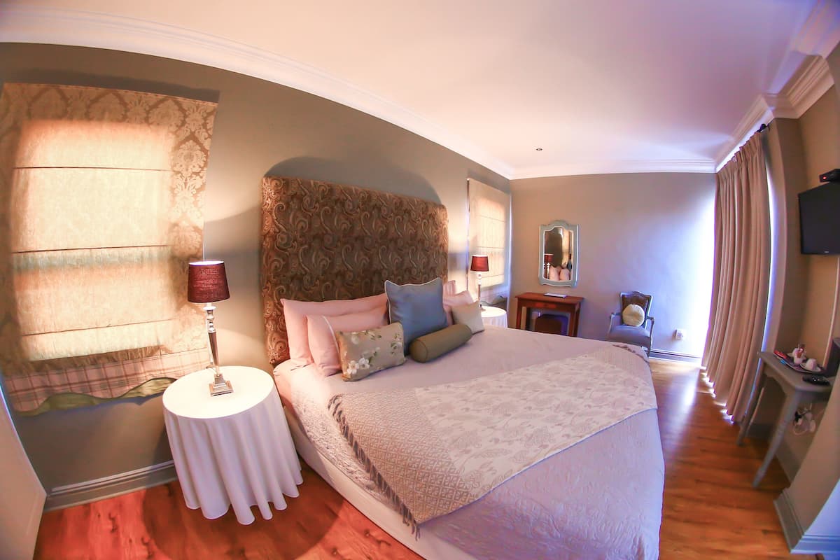 A bedroom with a large bed, a bedside table, a lamp, a mirror, and a TV.