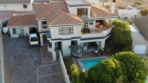 Una casa de dos pisos con piscina, un porche cubierto y un coche estacionado en la entrada.