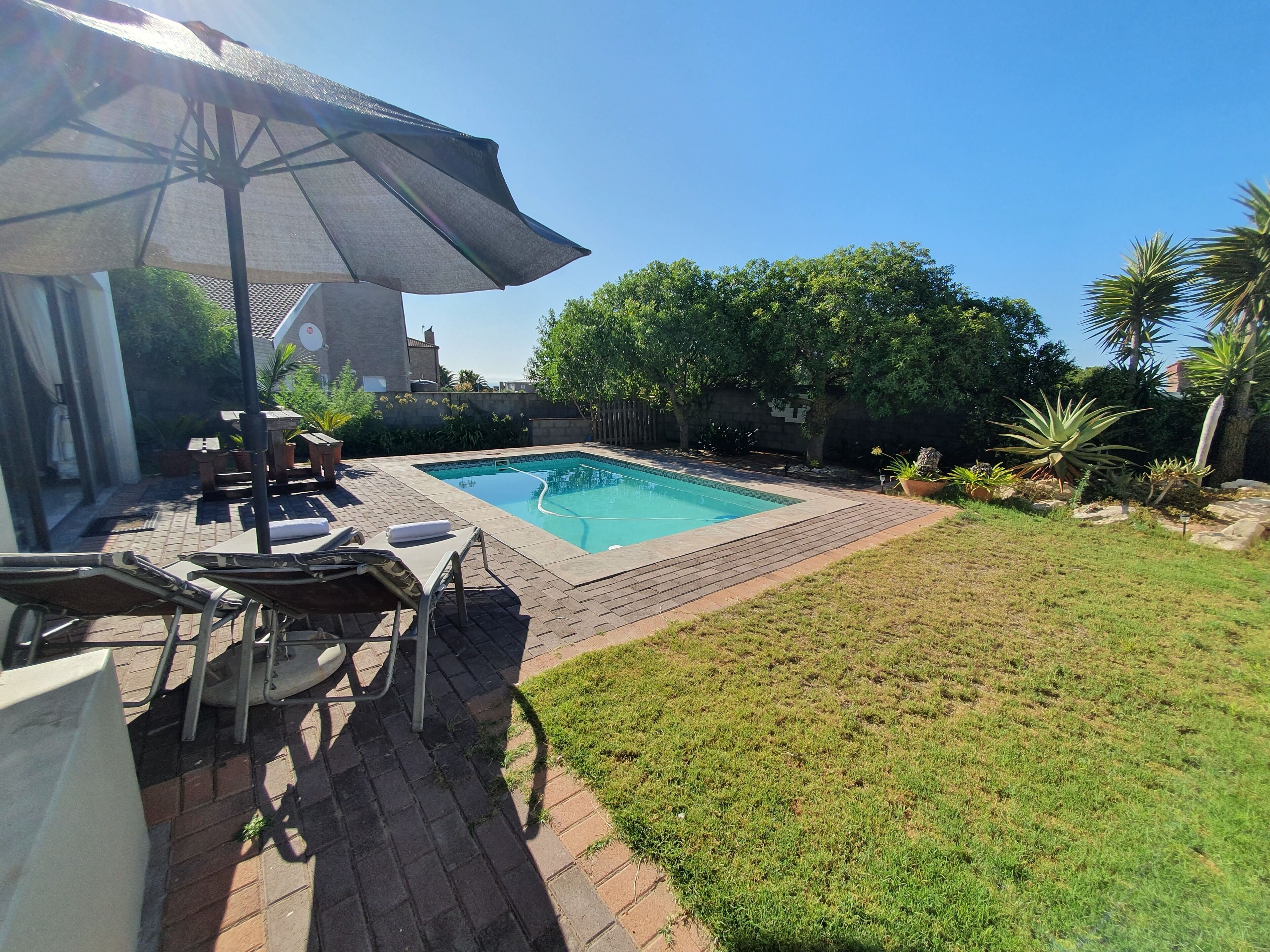 A backyard with a swimming pool, patio furniture, and a large umbrella.