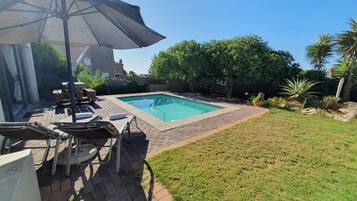 Patio trasero con piscina, muebles de jardín y una sombrilla grande.