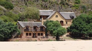 A two-story building with a balcony and a flat roof, surrounded by greenery and a sandy area. - Tides Lodge (Malagas)