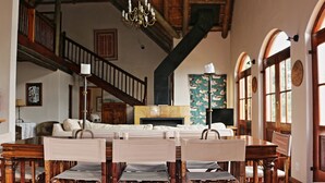A spacious living room with a high ceiling, wooden beams, a fireplace, and a staircase. - Tides Lodge (Malagas)