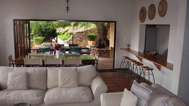 A modern living room with a white sofa, a dining area with a table and chairs, and a kitchen area with bar stools. - Tides Lodge (Malagas)