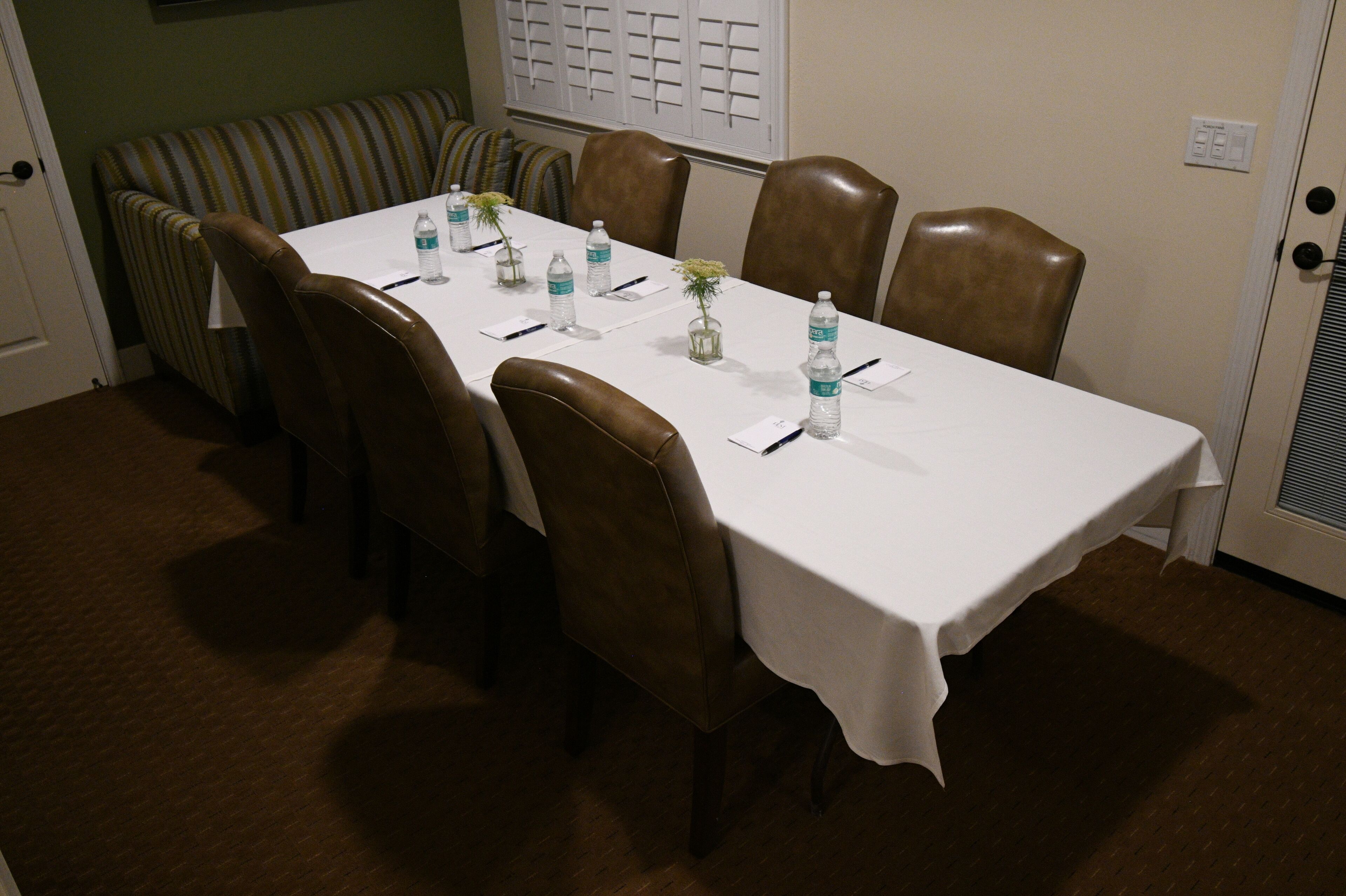 A conference room with a long table, brown leather chairs, and a striped bench.