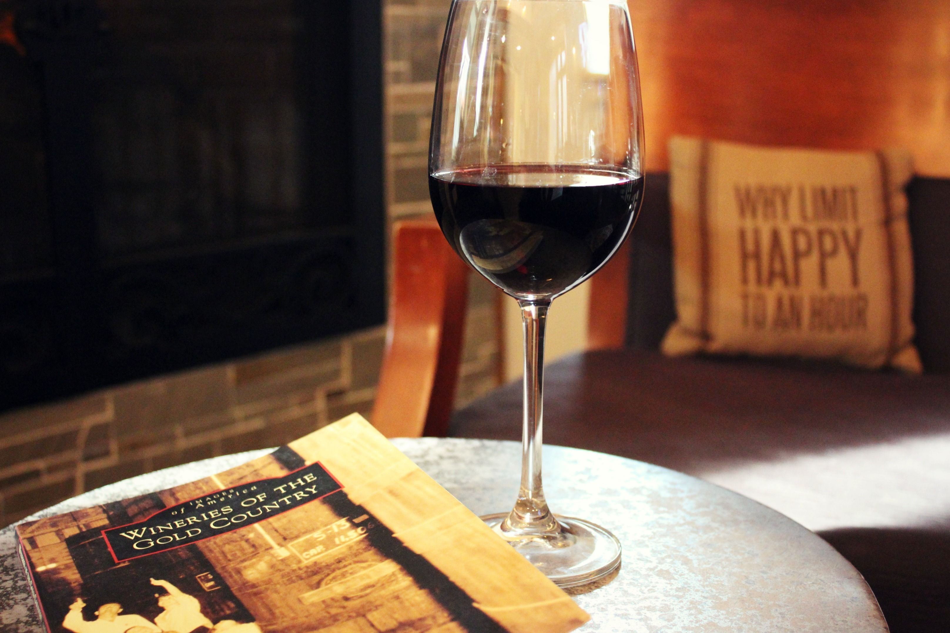 Un verre de vin rouge sur une table ronde, à côté d'un livre intitulé « Les vignobles de la région aurifère ».