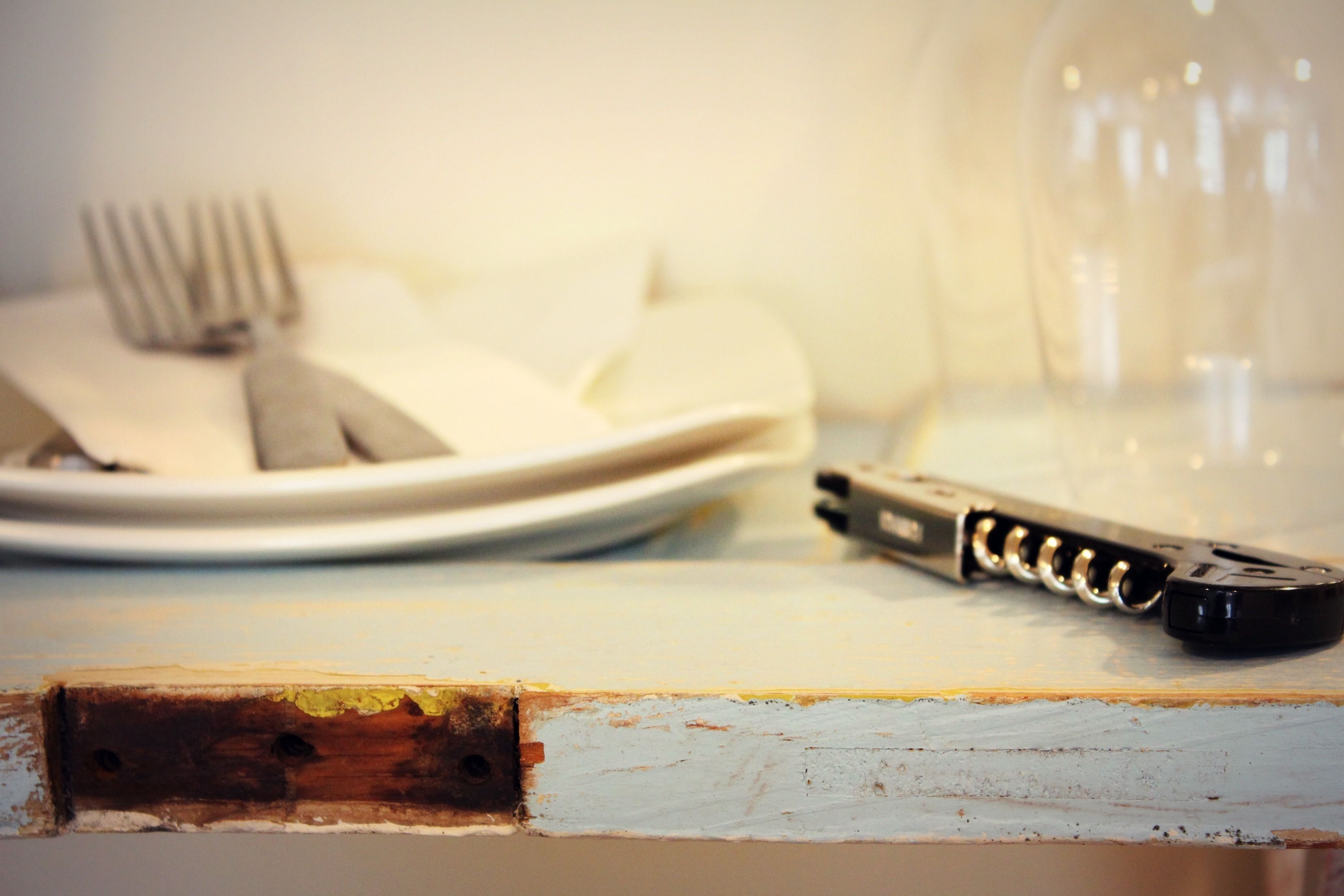 Uma mesa de madeira rústica com um abridor de garrafa e um garfo num prato.