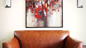 A brown leather sofa in a room with a large abstract painting on the wall.