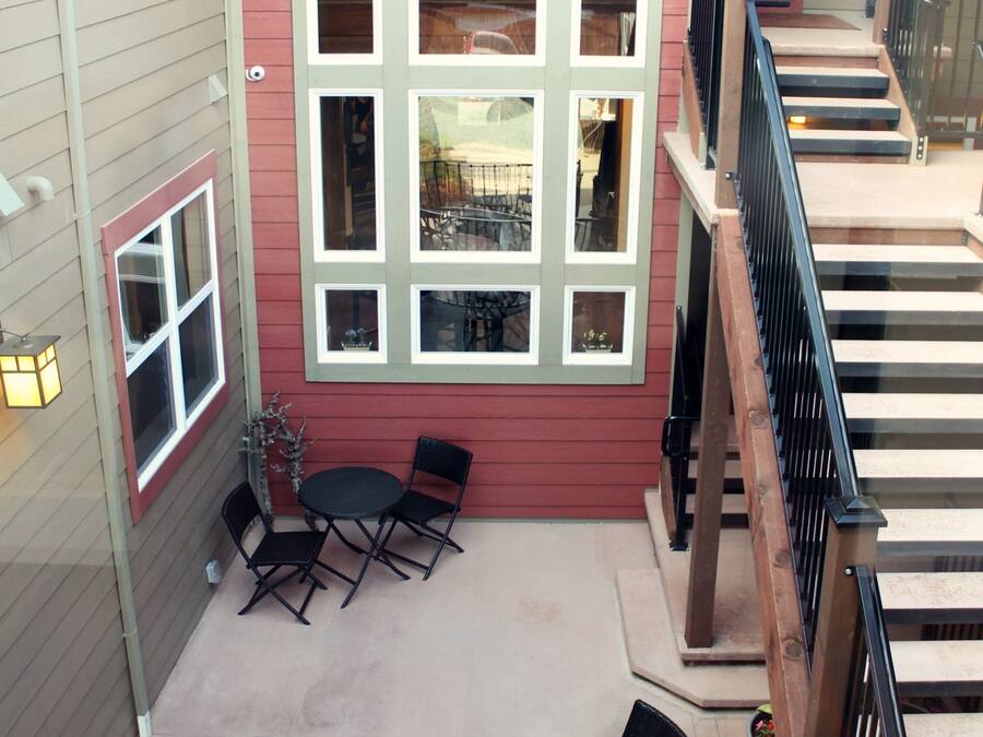 Een overdekt terras met een tafel, stoelen, een trap en een uitzicht op het interieur door grote ramen.