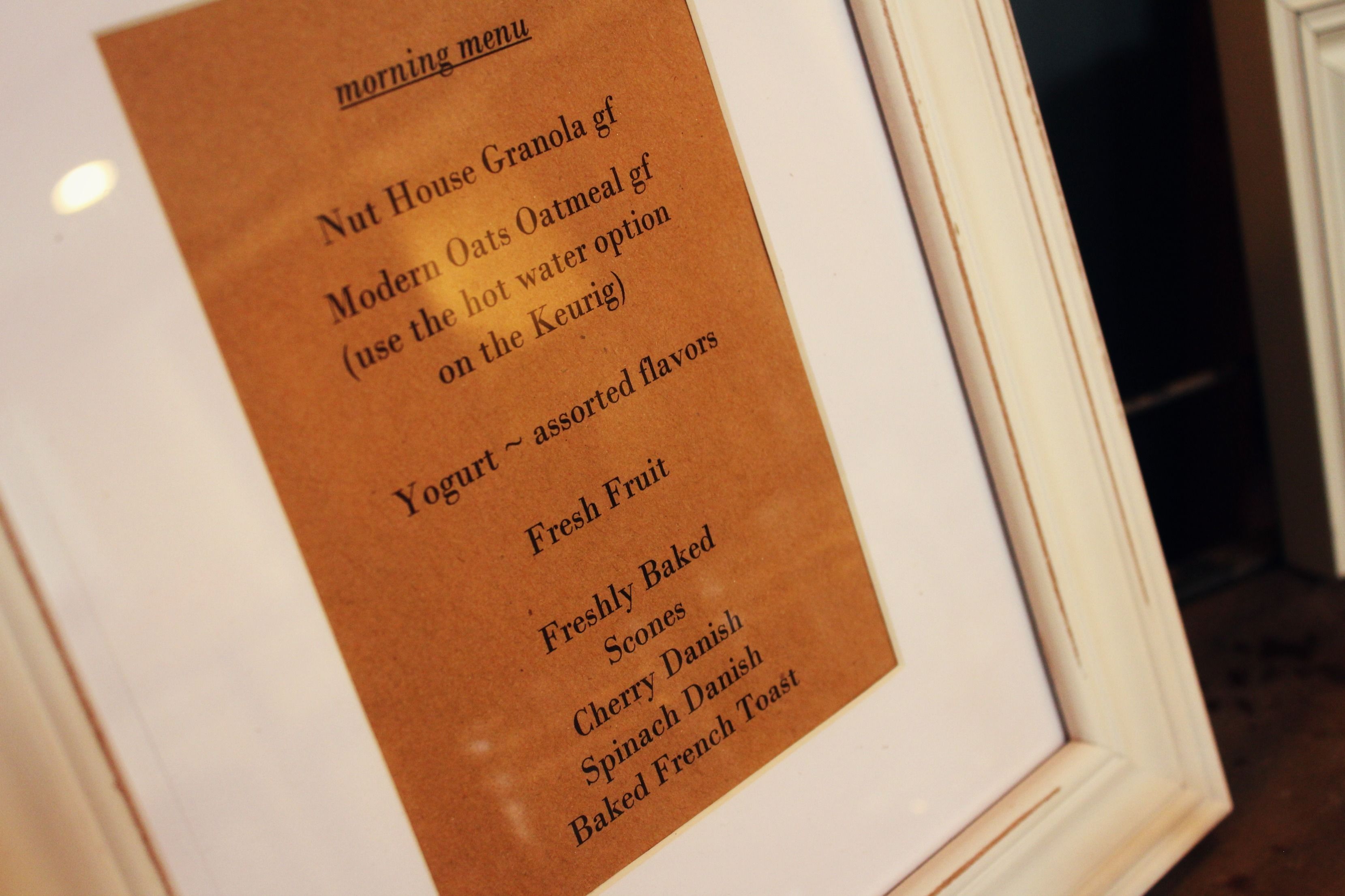 A framed menu listing breakfast options including Nut House Granola, Modern Oats Oatmeal, Yogurt, Fresh Fruit, Freshly Baked Scones, Cherry Danish, and Baked French Toast.