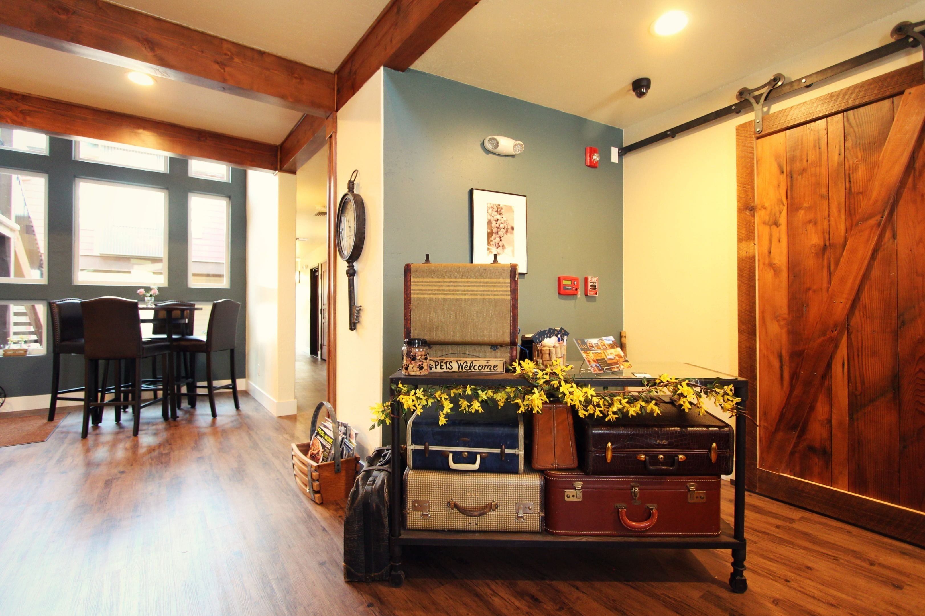 A dining area with a wooden table and chairs, a wall-mounted clock, and a wall with a framed picture and a sign.