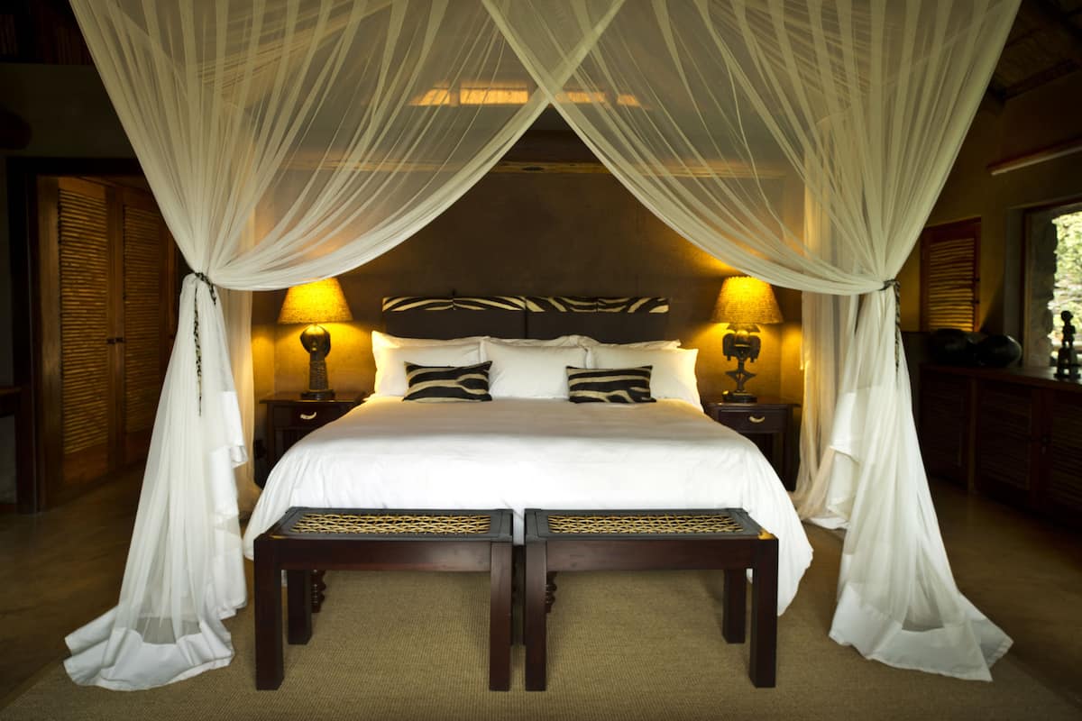 A large bed with a canopy, two bedside lamps, and a headboard with a zebra pattern.