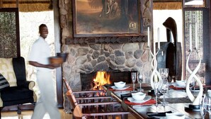 Un comedor con chimenea de piedra, mobiliario de madera y techo de paja.
