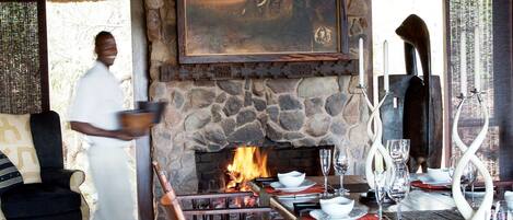 Un comedor con chimenea de piedra, mobiliario de madera y techo de paja.