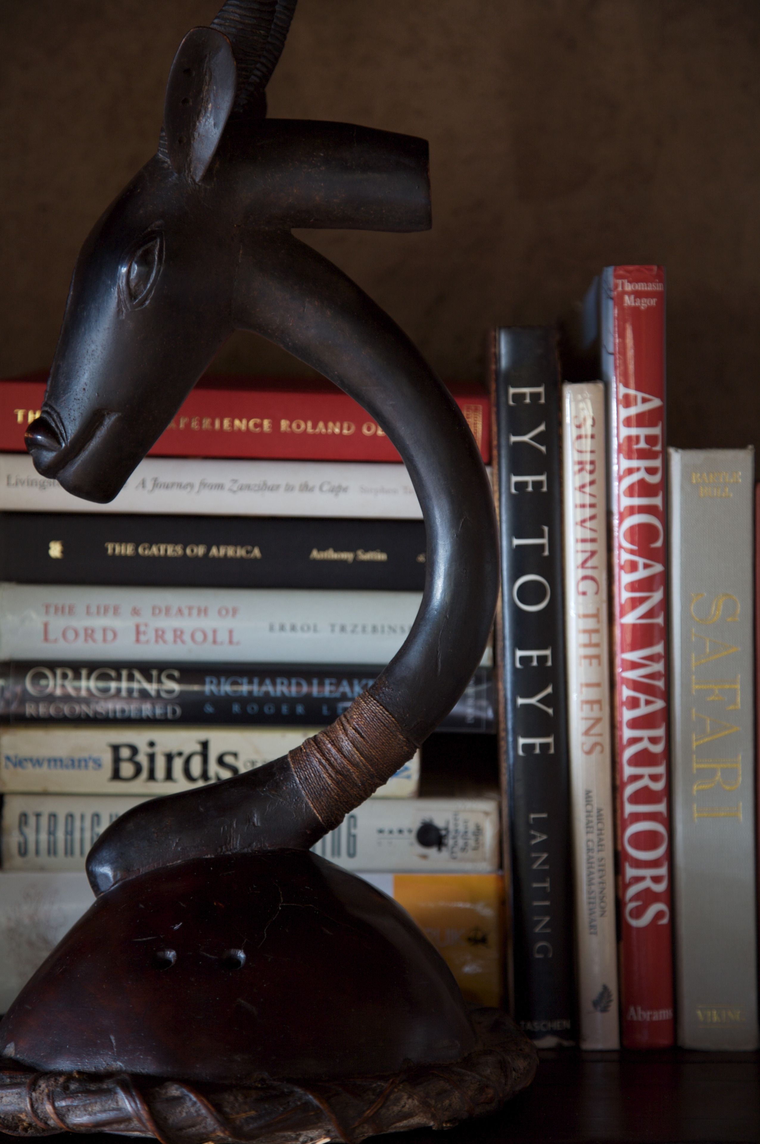 Uma escultura de gazela sobre uma estante com livros.