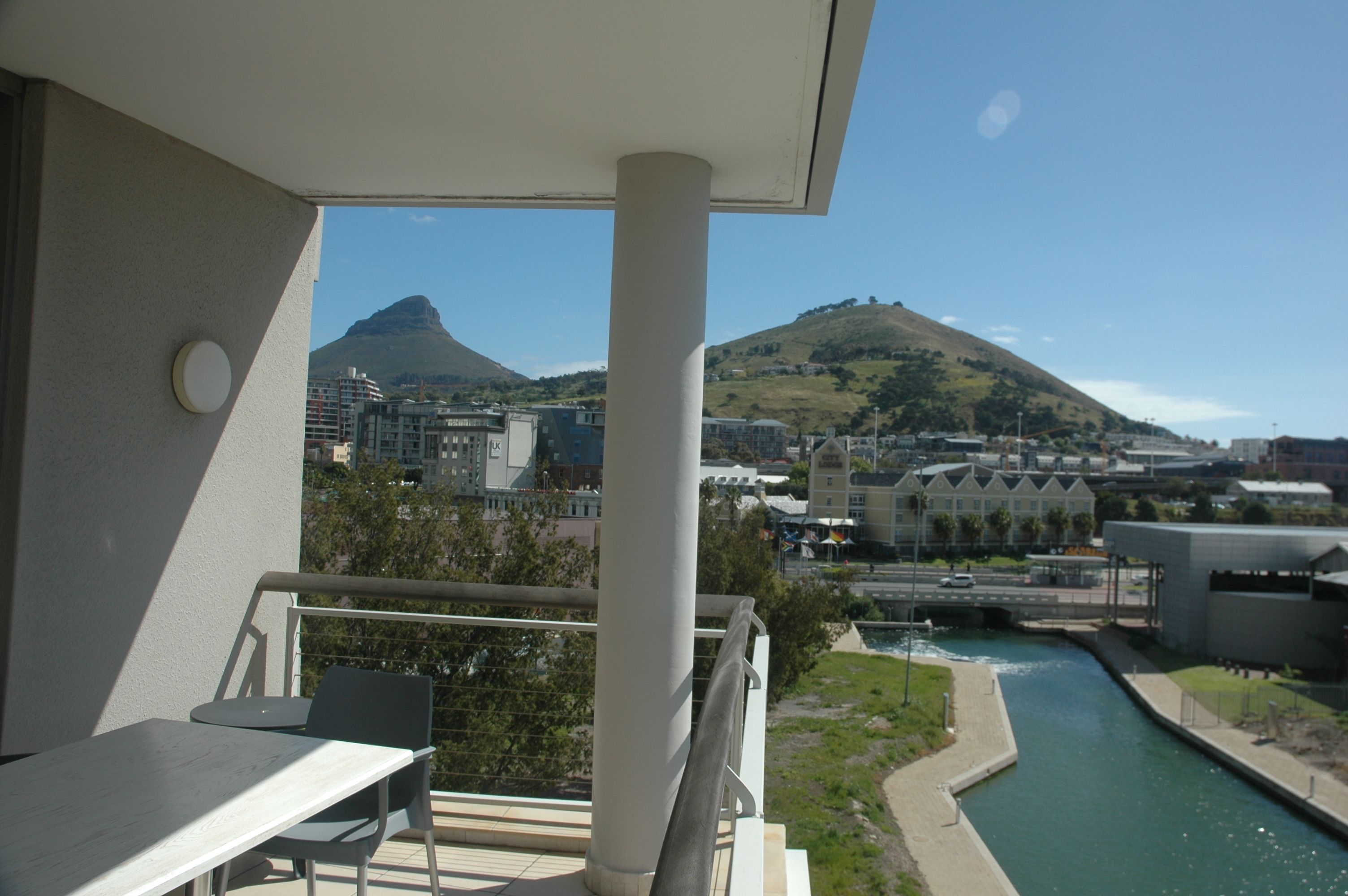 Ein Balkon mit Tisch und Stühlen, mit Blick auf einen Fluss und Gebäude, im Hintergrund ein Berg.