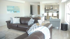 A modern living room with a brown leather sofa, a grey armchair, and a dining area with a glass table. - 501 Canal Quays (Cape Town)