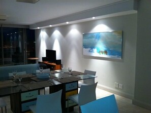 A modern dining area with a glass table, white chairs, and a painting on the wall. - 501 Canal Quays (Cape Town)