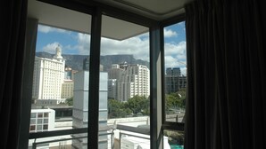 A view from a window with curtains, overlooking a cityscape with several high-rise buildings and a mountain in the background. - 501 Canal Quays (Cape Town)