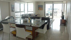 A modern dining area with a glass-top table, white chairs, and a central island with a bottle and glasses. - 501 Canal Quays (Cape Town)