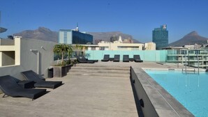 A rooftop pool area with lounge chairs, a swimming pool, and a view of city buildings and mountains. - 501 Canal Quays (Cape Town)