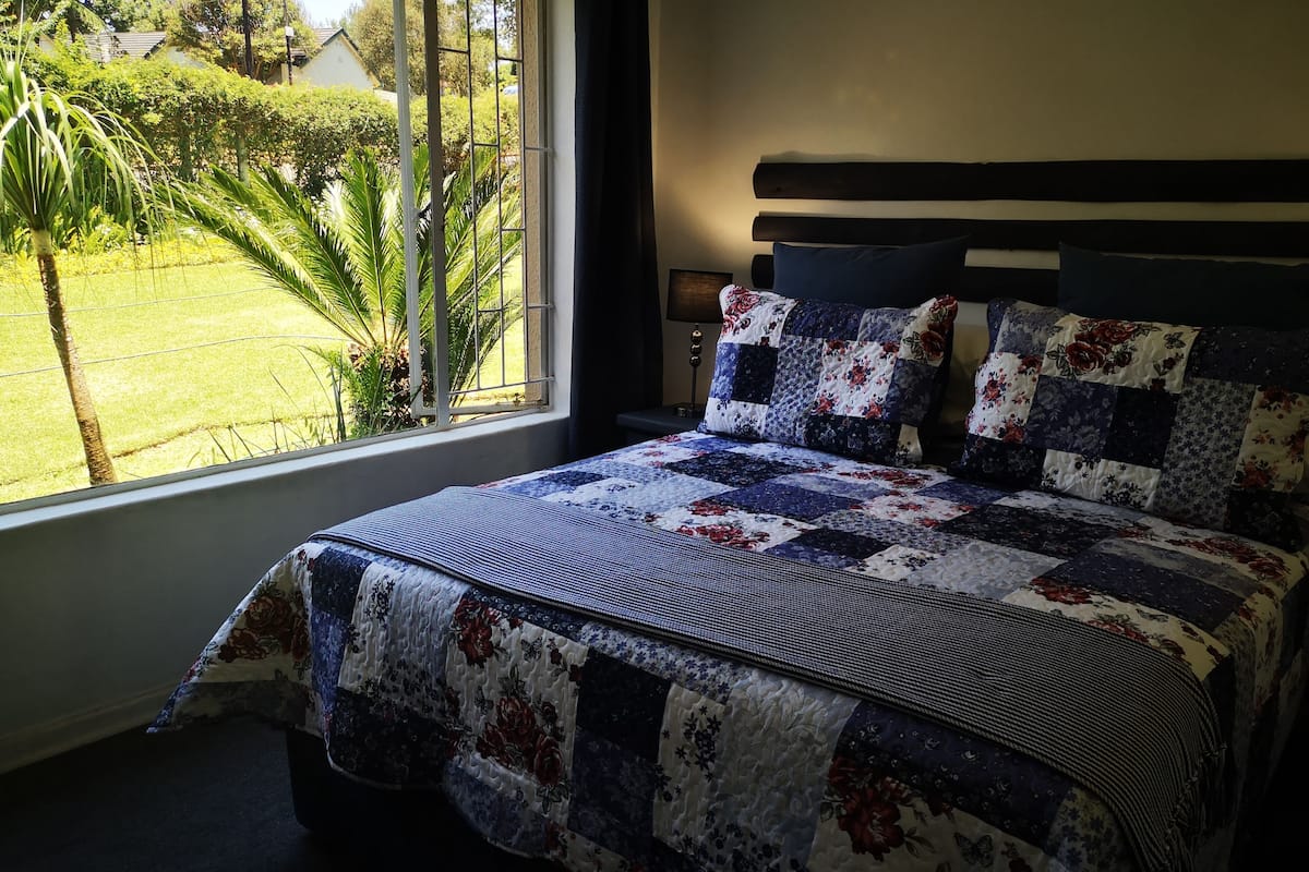 Un dormitorio con un ventanal grande, una cama con ropa de cama floral y vistas a la vegetación exterior.