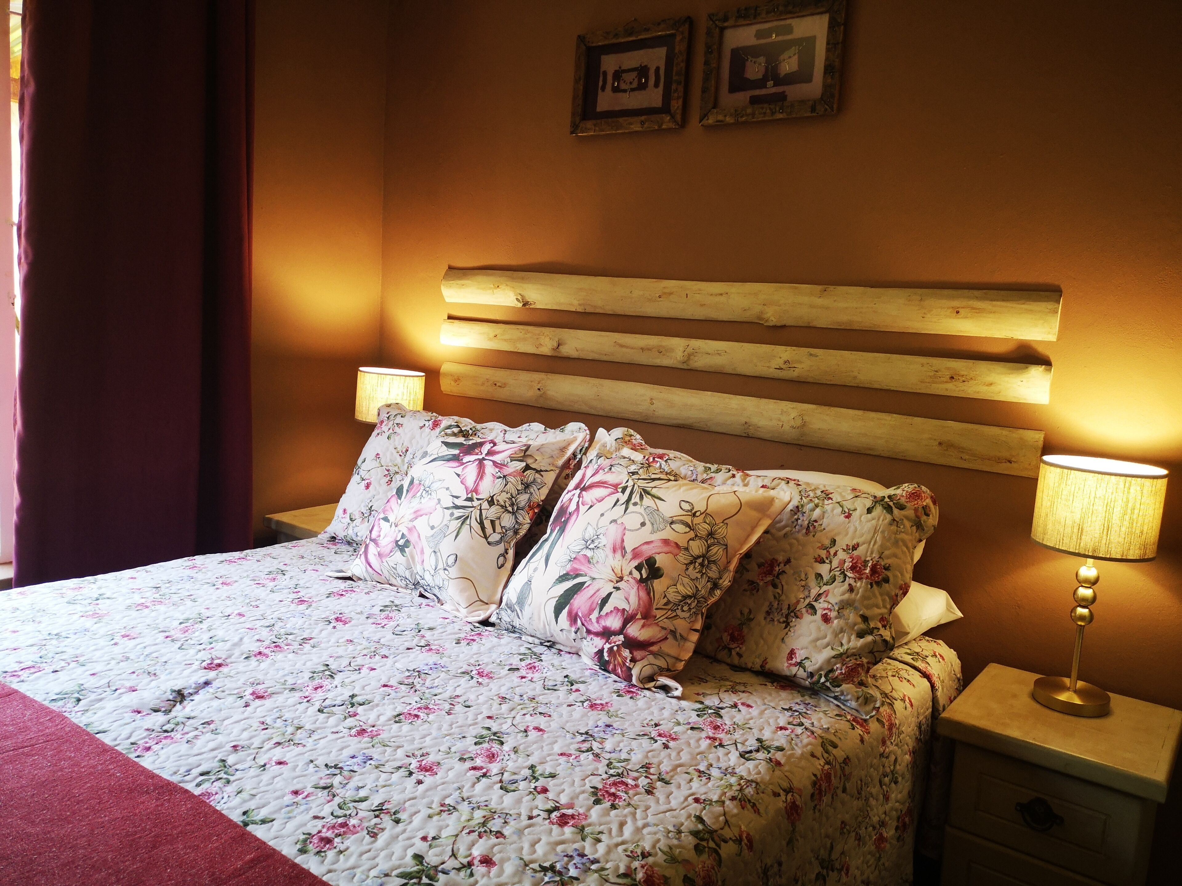A bed with floral bedding, wooden headboard, two bedside lamps, and a nightstand with a drawer.