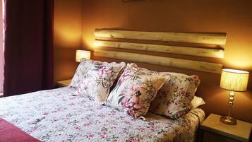 Uma cama com roupa de cama floral, cabeceira de madeira, duas luminárias de cabeceira e uma mesa de cabeceira com gaveta.