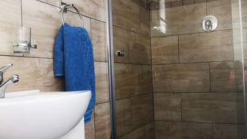 Un baño con un lavamanos blanco, una toalla azul, una cabina de ducha de vidrio y una planta en maceta.