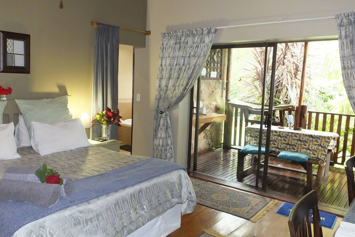 Habitación de hotel con una cama grande, una mesita con sillas y un balcón con mesa y sillas.