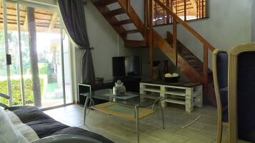 Una sala de estar con una televisión, una mesa de centro de vidrio, un sofá y una escalera.