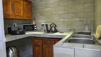 A kitchen with wooden cabinets, a microwave, kettle, and a sink.