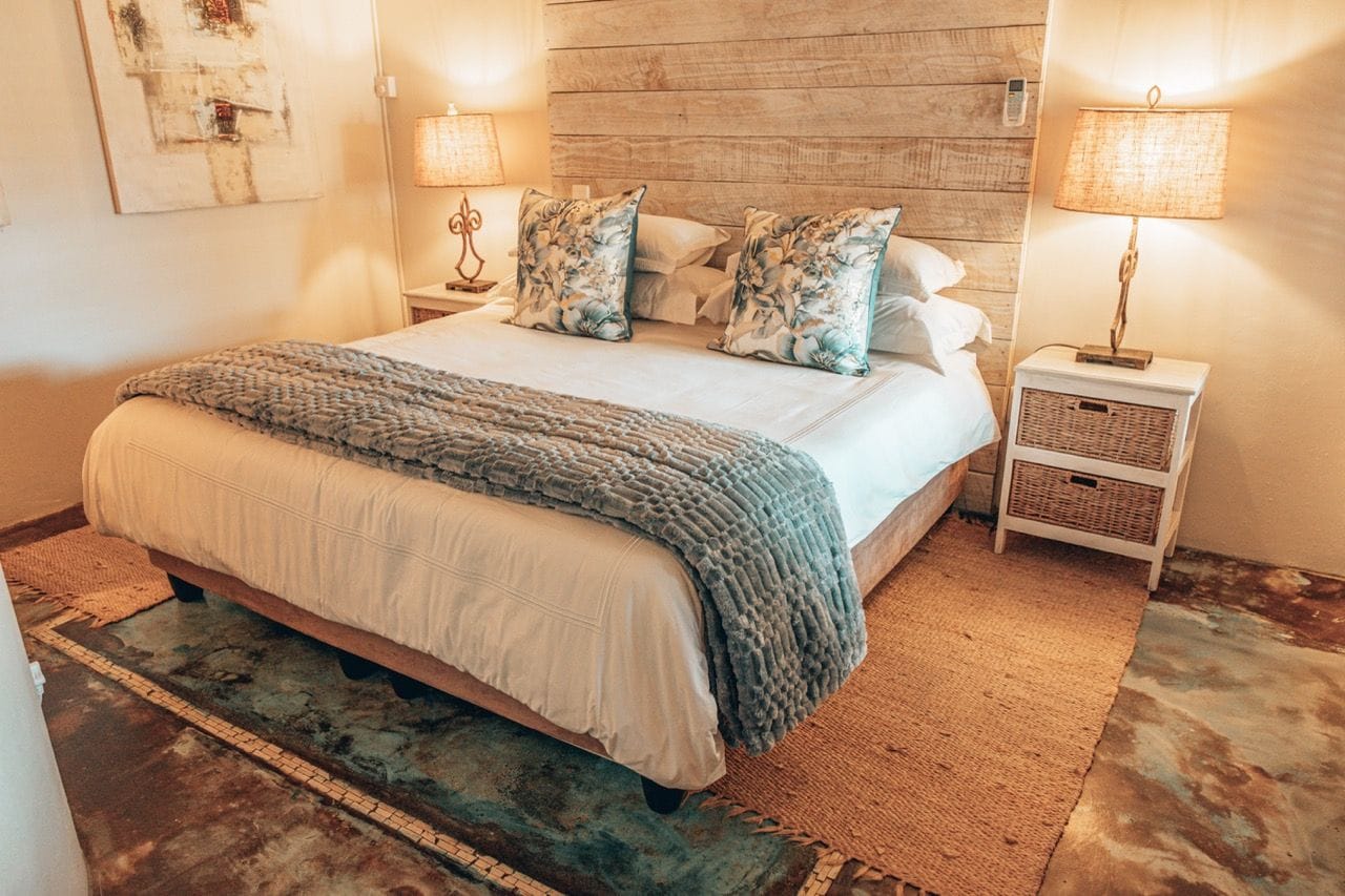 A bedroom with a large bed, two bedside tables with lamps, a wooden headboard, and a rug.
