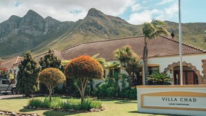 Villa Chad, a luxury guesthouse with a tiled roof, surrounded by well-maintained gardens and a mountain backdrop. - Villa Chad Luxury Guesthouse (Kleinmond)