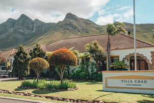 Villa Chad, una casa de huéspedes de lujo con techo de tejas, rodeada de jardines cuidados y un paisaje montañoso.