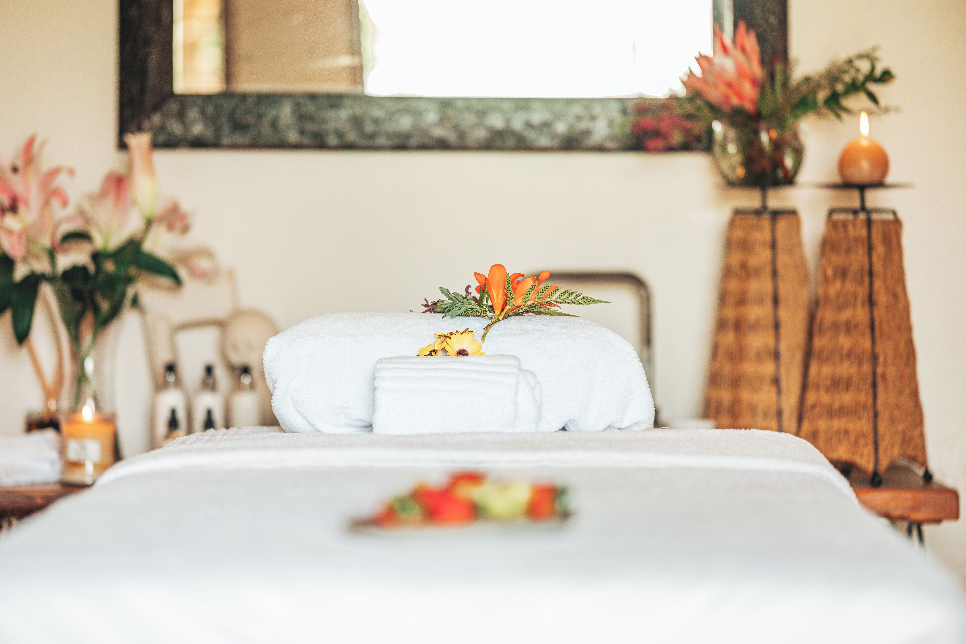 A neatly made bed with white linens, a decorative flower arrangement, and a candle on a bedside table.